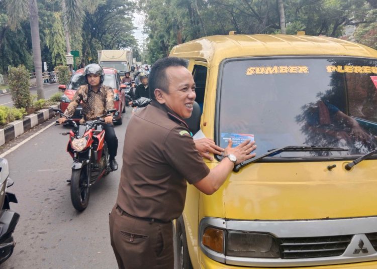 Kajari Kabupaten Cirebon, Yudhi Kurniawan, saat menempelkan stiker anti korupsi ke angkutan umum yang melintas di perempatan lampu merah kawasan Kecamatan Sumber, Kabupaten Cirebon, Senin (9/12/2024). /* (foto: M. Rahmat) 