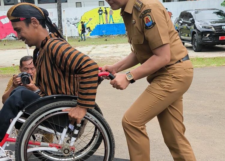 Pj Bupati Cirebon, Wahyu Mijaya, membatu seorang penyandang disabilitas dalam Peringatan Hari Disabilitas Internasional tingkat kabupaten yang digelar oleh Forum Komunikasi Difabel Cirebon (FKDC) di Kantor Kecamatan Lemahabang, Selasa (3/12/2024). /* (foto: Prokompim)